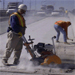 Construction Safety by National Institute for Occupational Safety and Health. Two men working on a highway with heavy construction equipment and dust in the air.